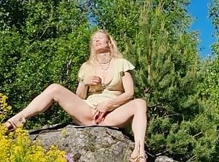 Horny MILF masturbating in a summer dress on top of a huge rock in a public park at midsummer